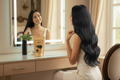 Woman with long hair admiring herself in a mirror with a product box on the vanity.